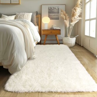 Cozy bedroom with a fluffy white rug, bed, nightstand, and decorative plants.